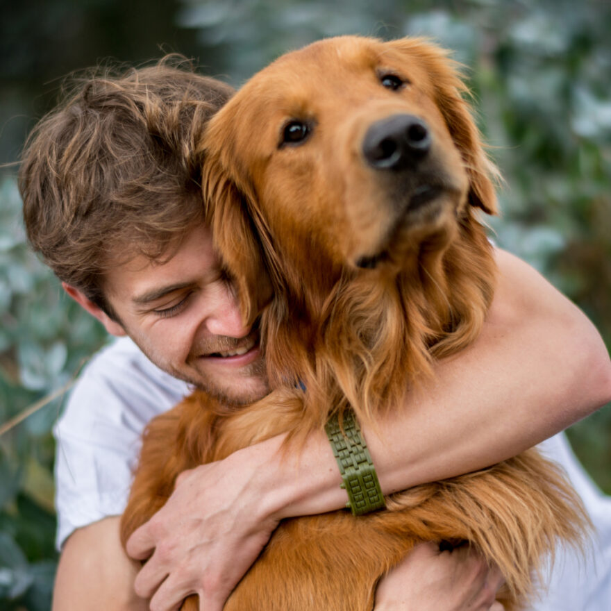 Loving man outdoors hugging his Golden Retriever dog and looking very happy